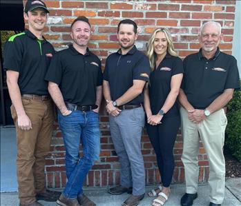 four men and one woman in SERVPRO uniforms standing in front of brick wall