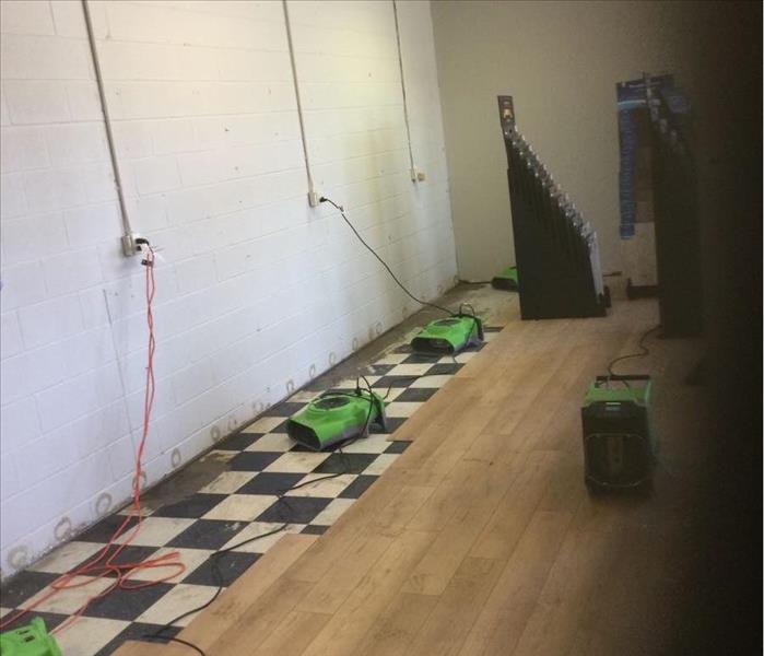 room with some wood flooring removed exposing black and white tile with drying equipment placed
