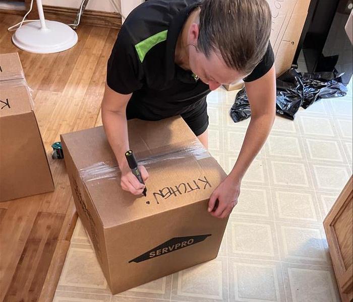man in black shirt writing kitchen on servpro labeled cardboard moving box