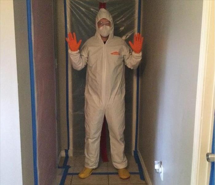 person wearing white tyvek suit, orange gloves, and mask